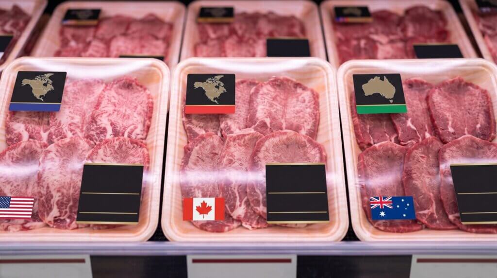 日本の食肉卸売市場で、海外の巨大パッカーから届いた大量の外国産牛タンの真空パックが段ボールから運び出される様子。需給構造を支える輸入流通网。
