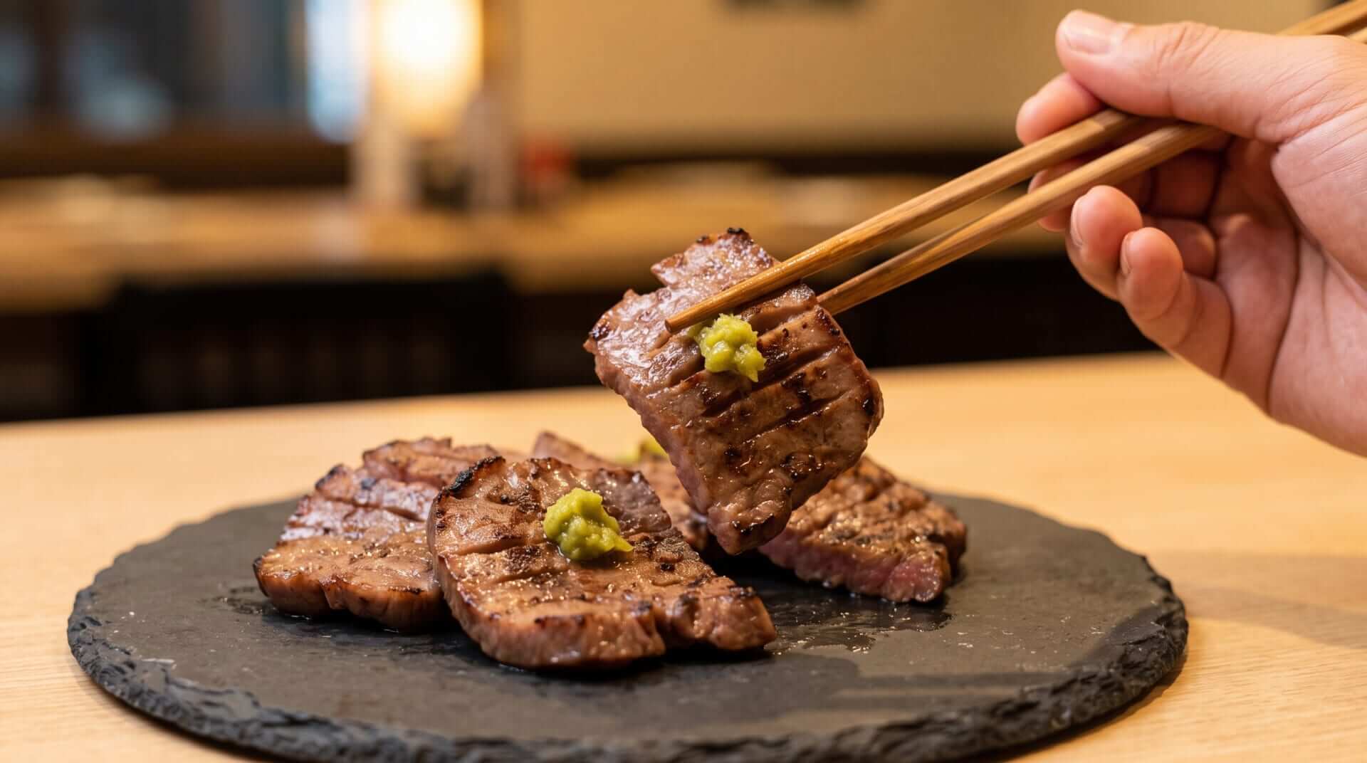 スレートプレートに盛られた、焼き目の美しい牛タンの塩焼き。一切れを箸で持ち上げ、鮮やかな緑色の柚子胡椒が乗せられている至高の組み合わせの瞬間。