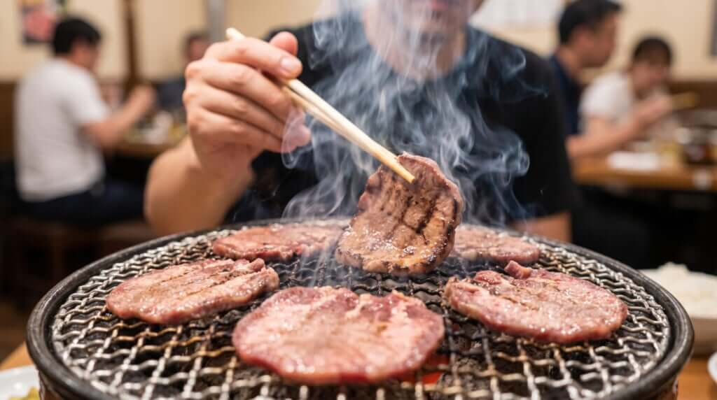 焼肉店の網の上で焼かれる牛タンと立ち上る煙、日本の焼肉体験。