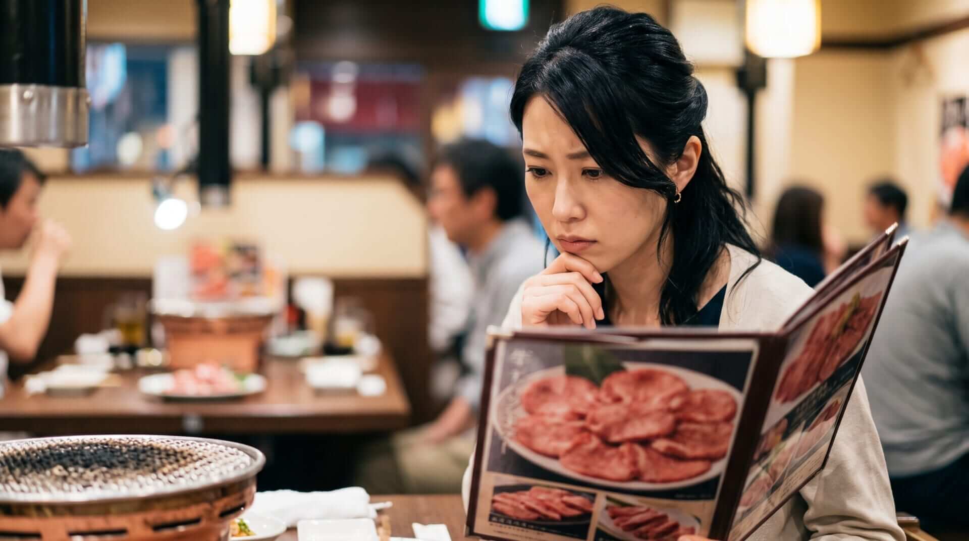 焼肉店でメニューの牛タンの写真を見つめる日本人女性